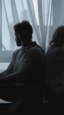 Hafifçe aydınlatılmış bir odada, genç bir çift sırt sırta oturur, siluetleri yakınlardaki bir pencerenin nazik parıltısıyla hafifçe çizilir. Karşıt yönlere bakarken başları hafifçe dokunur, hassas bir bağlantı anını yakalar ve...