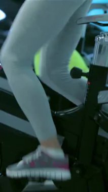 Güçlü bacakları olan atletik bir kız, dört formda arkadaşı tarafından çevrelenmiş, durgun bir bisikletin üzerinde enerjik bir şekilde pedal çeviriyor, hepsi de yüksek enerjili bir egzersize dalmış. Spor salonu motivasyon ve arkadaşlıkla uğulduyor. Kararlılıklarını ve güçlerini gösteriyor.