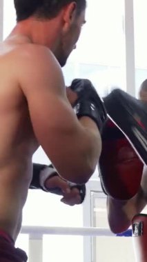 Çarpıcı bir dikiz aynası, güçlü kaslı bir erkek boksörün odaklanmış antrenman ortağının tuttuğu pedlere sert bir yumruk attığını gösteriyor. Parlak, enerjik jimnastik salonu bu hareketli antrenman seansının şiddetini arttırıyor.