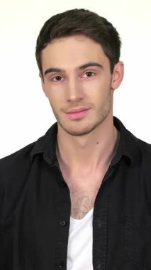 Kendine güvenen genç bir adam, yumuşak beyaz bir arka plana karşı duruyor, kollarını kavuşturmuş, siyah bir gömlekle cazibe saçıyor. Onun sıcak gülümsemesi ve çekici bakışları davetkar bir atmosfer yaratıyor, modern erkeksiliği ve gayretsiz stili somutlaştırıyor.