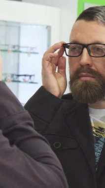 Sakallı, olgun bir adam şık gözlük dükkanındaki yansımasına bakarken şık gözlükleri incelikle ayarlar. Bu canlı sahne, hem güveni hem de özel yeteneği yansıtıyor. Her iki görüşü de geliştirmek için mükemmel bir aksesuar seçmenin hazzını gösteriyor.