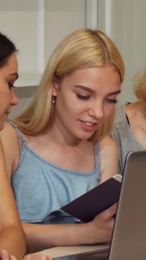 Canlı üç genç kadın parlak bir dizüstü bilgisayarın etrafında toplanıyor, bir kitabı hevesle paylaşıyorlar ve canlı bir üniversite ortamında parlak fikirler alışverişinde bulunuyorlar. Işıl ışıl gülüşleri ve hareketli ifadeleri takım çalışmasının ve akademik heyecanın keyfini yansıtıyor.