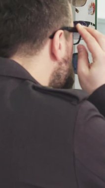 Sakallı, olgun bir adam şık bir gözlükçüdeki yansımasına bakarken şık gözlükleri incelikle ayarlar. Bu canlı sahne, hem vizyonu hem de kişisel stili geliştiren mükemmel aksesuarı keşfetmenin heyecanını özetliyor.