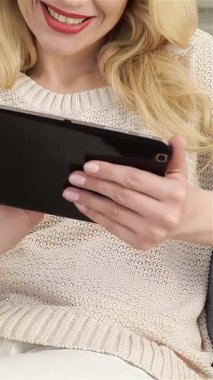 Çekici sarışın bir kadının hoş bir yakın çekimi. Tabletiyle dolu şık bir sandalyede rahatlarken neşe saçıyor. Sıcak gülüşü ve rahat tavırları modern teknolojiyi sakin ve rahat bir ortamla harmanlayan davetkar bir atmosfer yaratıyor.