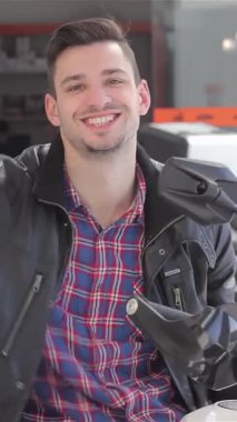 Şık bir deri ceket giymiş neşeli bir esmer adam galeride bulaşıcı bir heyecanla motosiklet anahtarlarını sallıyor. Pürüzsüz beyaz bir motosikletin üzerinde güvenle otururken, yeni maceraların heyecanını somutlaştırıyor.