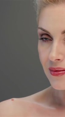 Büyüleyici sarışın bir kadın büyüleyici bakışlarıyla büyülüyor. Kusursuz cildi, yumuşak, gri bir arka planda parlıyor. Bu portre zarafet ve güzelliği özetliyor. Nazik gülüşünü ve narin yüz hatlarını vurguluyor. Seyircileri davet ediyor.