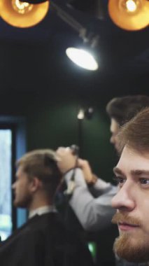 Sıcak, davetkar ışıklarla aydınlatılan modaya uygun bir berber dükkanında yetenekli bir berber, bakımlı sakallı genç bir adama şık bir saç kesimi yapmaya odaklanıyor. Atmosfer güven ve rahatlama ile uğulduyor.