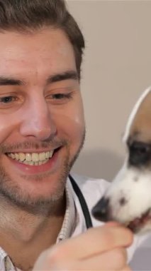 A cheerful young male veterinarian feeds a joyful Jack Russell Terrier in a bright, welcoming veterinary clinic. The dogs eager, gentle licking of the vets hand radiates warmth and affection, showcasing their strong bond in a nurturing environment