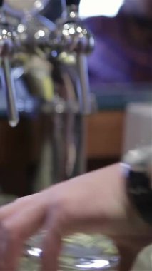A close-up of a skilled male barmans hand elegantly pouring a golden lager from a gleaming tap into a frosty glass mug, forming a perfect frothy head. This vibrant scene encapsulates the lively bar atmosphere, highlighting the artistry of bartending