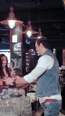In a lively bar bathed in warm, inviting light, two cheerful young women and a smiling man eagerly await their drinks from a friendly bartender. Their infectious laughter and animated chatter create a vibrant atmosphere, celebrating friendship and