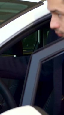 A stylish young man with a well-groomed beard sits confidently in a modern car at the dealership, his thoughtful expression reflecting excitement for new beginnings. The bright, polished interior gleams around him, enhancing the atmosphere of