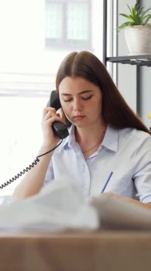 A dedicated young female designer is deeply immersed in a phone conversation, showcasing her professionalism in a chic, modern office. The vibrant workspace, filled with creative energy, highlights her commitment to fashion and collaboration, while a