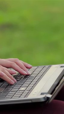 A cheerful girl is deeply engaged in typing on her laptop, nestled among the lush greenery of a vibrant city park. This lively scene radiates youthful energy and the joy of productive leisure, as she basks in the warm sunshine and fresh air