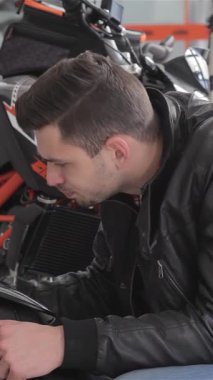 A close-up shot features a smiling Caucasian man in a stylish black jacket, giving a thumbs-up while admiring a sleek motorcycle. The vibrant dealership backdrop enhances the excitement, showcasing the bikes striking design and powerful front fork