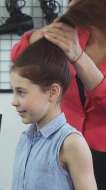 A joyful young girl with a charming smile sits in a salon chair as a skilled hairdresser expertly styles her hair, creating a vibrant and uplifting atmosphere. This enchanting scene captures the magic of childhood joy and the transformative