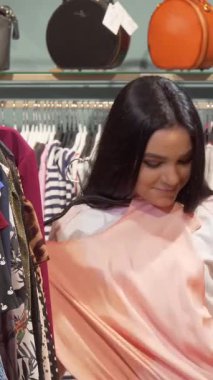 Two fashionable young women revel in a delightful shopping adventure, with one admiring a stunning dress while the other explores vibrant options nearby. The boutiques chic decor and colorful garments create an inviting atmosphere, perfect for a