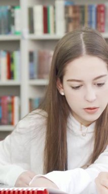 Two dedicated teenage girls are deeply engaged in their studies at a lively library, surrounded by colorful bookshelves. Their expressions radiate concentration and joy, showcasing the essence of teamwork and friendship in an inspiring academic
