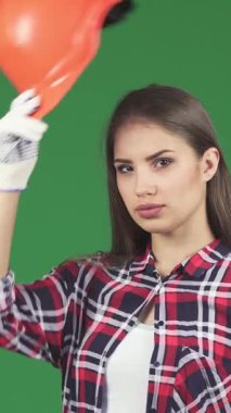 A confident young female contractor, adorned in a vibrant orange hardhat and stylish gloves, gives a thumbs up against a lively green chromakey background. Her playful smile exudes empowerment and professionalism, showcasing the dynamic spirit of