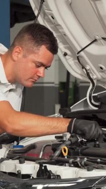 A cheerful young mechanic smiles brightly while skillfully inspecting the engine of a sleek car in a lively garage. Surrounded by an array of tools and the energetic buzz of automotive activity, his passion and expertise shine through, embodying the