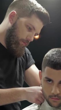 Şık bir berber dükkanında, şık sakallı uzman bir berber genç bir erkek müşteri için mükemmel saç kesimi ve sakal kesimi üzerine odaklanır. Enerjik atmosfer enerji ile uğulduyor, modern tımarcılığın ustalığını ve hassasiyetini vurguluyor.
