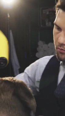 Çekici bir berber dükkanında şık bir yelek giymiş, şık bir genç berber müşterilerinin saçlarını ustalıkla kurutuyor, yeteneğini ve yeteneklerini sergiliyor. Yumuşak ışıklandırma ve klasik dekorla vurgulanan sıcak, davetkar atmosfer samimi bir ortam yaratır.