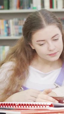 Üç neşeli genç kız, bir proje üzerinde çalışırken akıllı telefonlarına dalmış, rahat bir okul kütüphanesinde kahkahalarını paylaşıyorlar. Enerjileri ve günlük kıyafetleri, arkadaşlığın ve takım çalışmasının güzelliğini vurgulayan canlı bir atmosfer yaratıyor.