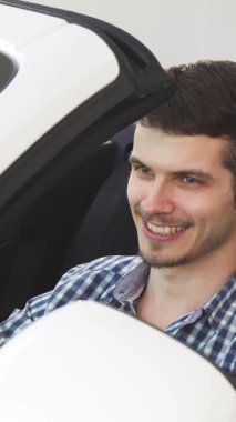 Işıldayan genç bir adam, üstü açık şık beyaz arabasında otururken kendinden emin bir şekilde arabasının anahtarlarını sergilerken mutluluk saçıyor. Bu canlı sahne, yeni sahipliğin coşkusunu ve açık yolun özgürleştirici ruhunu özetliyor.