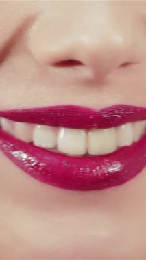 Bu büyüleyici yakın plan güzel genç bir kadının büyüleyici, ışıltılı dudaklarını göz kamaştırıcı bir gülümsemeyle aydınlatıyor. Kusursuz cildine ve canlı rujunun ışıldayan ışıltısına odaklanması davetkar bir atmosfer yaratıyor.