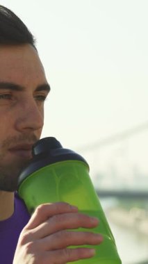 Yakından çekilen bir fotoğraf, sağlıklı bir delikanlıyı açık hava egzersizinden sonra canlı yeşil bir su şişesiyle neşe içinde yakalar. Işıl ışıl gülüşü ve odaklanmış ifadesi zindelik ve refahı yansıtıyor, canlandırıcı gücünü gösteriyor.