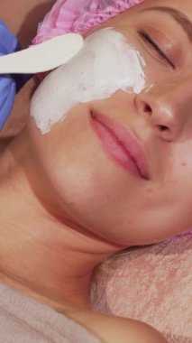 Mutluluk dolu genç bir kadın, sakin bir güzellik kliniğinde gözleri nazikçe kapalı, rahatlatıcı bir yüz maskesi uygulamasının tadını çıkararak rahatlar. Yetenekli güzellik uzmanları eldiveni nazikçe taktılar. Maskeyi taktılar. Işıl ışıl cildini geliştirdiler.