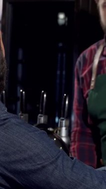 Tarz sahibi sakallı tanınmayan bir adam, parlak bir bardakta zengin bir zanaat birasının tadını çıkarırken, yeşil önlüklü dost canlısı bir barmen ustalıkla içki servisi yapıyor. Yumuşak ışığın sıcacık parıltısı ve barın canlı atmosferi