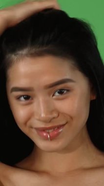 Bu canlı stüdyo portresi çarpıcı bir dudak halkası ile neşeli genç bir Asyalı kadını yakalıyor, uzun, parlak saçlarını canlı yeşil bir krom arka planda şaklatarak çeviriyor. Işıl ışıl gülüşü ve etkileyici gözleri özgüven ve cazibe saçıyor.