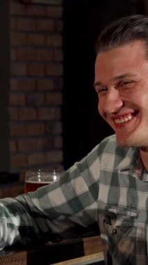 Çekici genç bir çift, sıcak bir barda, ellerinde buzlu bir bardak bira olan heyecanlı bir sohbeti paylaşıyor. Yakışıklı adam, şık bir saç kesimi ve ekose gömleği ile, gülüşmeler ve flört ederken sıcaklık ve bağlantı yayıyor.