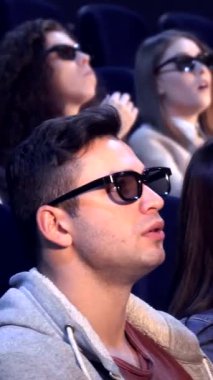 Üç boyutlu gözlük takan çeşitli genç yetişkinlerden oluşan bir grup, rahat bir sinemada canlandırıcı bir film karşısında büyüleniyor. Atmosfer, öne doğru eğildikçe heyecanla uğulduyor. Gözler açık, sinematik maceraya tamamen dalmış.