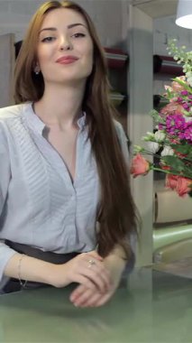 Genç, çekici beyaz bir çiçekçi zarif bir şekilde şık masasına eğiliyor, hareketli çiçekçi dükkanında sıcaklık ve yaratıcılık saçıyor. Göz kamaştırıcı renkli çiçeklerle çevrelenmiş güzel kahverengi saçları büyülerken şelale gibi süzülüyor.