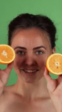 Işıldayan genç bir kadın mutluluk saçar, her iki elinde parlak turuncu yarımlar sunarak, canlı yeşil bir zemin oluşturur. Bu canlı görüntü sağlık ve canlılığın özünü özetliyor. Taze neşenin güzelliğini kutluyor.