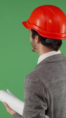 Parlak turuncu başlıklı erkek mühendisin dinamik arka görüntüsü canlı yeşil renkli bir ekrana doğru ustalıkla işaret ediyor. Bu büyüleyici sahne, ileri teknoloji ve yenilikçi mühendisliğin birleşiminin vücut bulmuş halidir.