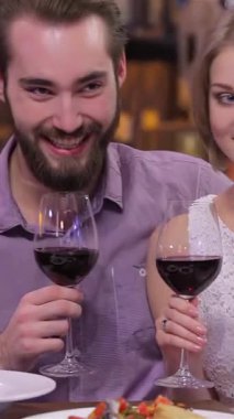 Zevkli bir nişanlı çift, romantik bir akşamda, sıcak bir restoranda şarap bardaklarını tokuşturup, aşklarını kutluyor. Yumuşak ışıklandırma ve zarif dekorlarla dolu samimi ortam, onların ışıl ışıl gülümsemelerini ve neşelerini arttırır.