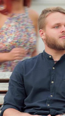 A joyful girl playfully covers her eyes while leaning in to kiss her partner, capturing a moment of pure affection at a vibrant urban beach. Their carefree spirits radiate warmth and happiness, surrounded by the lively city atmosphere and the golden