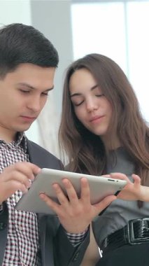 A thrilled young couple in stylish business attire eagerly examines impressive results on a sleek tablet, exuding joy and teamwork. Their radiant smiles and engaged expressions capture the vibrant spirit of entrepreneurship in a bright, modern office