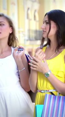 Three fashionable young women, each holding colorful shopping bags, stroll through a sunlit street, animatedly sharing their latest fashion discoveries. Their radiant smiles and infectious laughter create a vibrant atmosphere, embodying the joy of