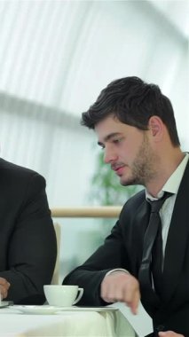 A vibrant team of four smiling businessmen actively collaborate in a sleek, sunlit office, exchanging ideas over coffee and documents. Their engaged expressions and animated discussions radiate a spirit of teamwork and innovation, showcasing a modern