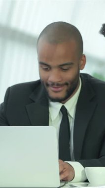 A diverse group of four enthusiastic young professionals engages in a lively discussion around a sleek, glass conference table, bathed in warm natural light from expansive windows. Their radiant smiles and animated gestures create an electrifying