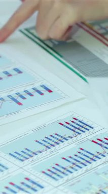 Canlı bir sahnede çeşitli eller aktif olarak iş belgelerindeki renkli grafik ve çizelgelere, somutlaştırıcı takım çalışması ve stratejik analizlere işaret ediyor. Bu büyüleyici görüntü, dinamik bir ofiste çalışan profesyonellerin sinerjisini vurgular.