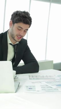 Two dynamic young businessmen, dressed in sharp formalwear, engage in an animated discussion at a modern table adorned with charts and a laptop. Their infectious smiles and enthusiastic gestures create an atmosphere of collaboration and innovation