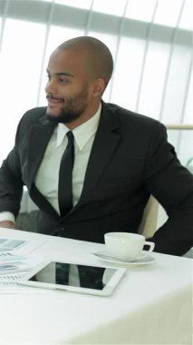 Two confident young businessmen, one with a stylish beard, share an animated discussion at a modern table, surrounded by vibrant charts and a sleek laptop. Their infectious smiles and dynamic energy create an atmosphere of collaboration and