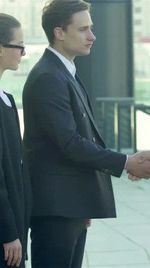 A dynamic trio of smiling business professionals in sleek black and white attire engage in a firm handshake on a sunlit city street. This vibrant scene radiates collaboration and success, capturing the thrill of forging new partnerships in the
