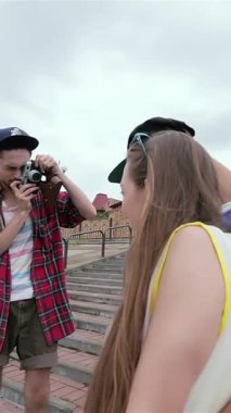 Three young men share infectious laughter on a lively urban street, as one friend joyfully snaps a photo with a vintage camera. This vibrant scene bursts with warmth and connection, perfectly encapsulating the spirit of friendship on a sunny day