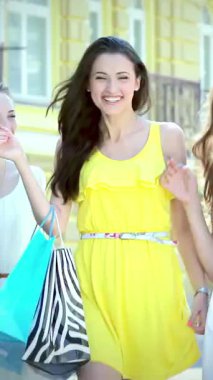 Three exuberant girls, radiating happiness in their vibrant outfits, confidently strut down a sunlit street, showcasing their chic shopping bags. Their infectious laughter and bright smiles embody the spirit of friendship and the thrill of a carefree