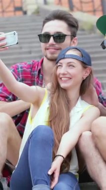 A vibrant trio of young friends, two men and a woman, joyfully pose on sunlit outdoor steps, capturing a selfie that radiates happiness. Their playful expressions and stylish summer outfits reflect the carefree spirit of friendship, creating